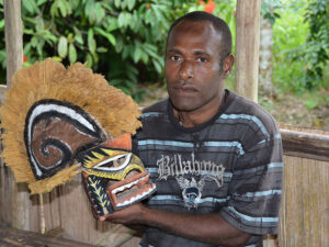 Ben Sisia jr., Sohn des Mastercarvers Ben Sisia, in Libba mit einer geschnitzten Maske. New Ireland, Papua Neuguinea